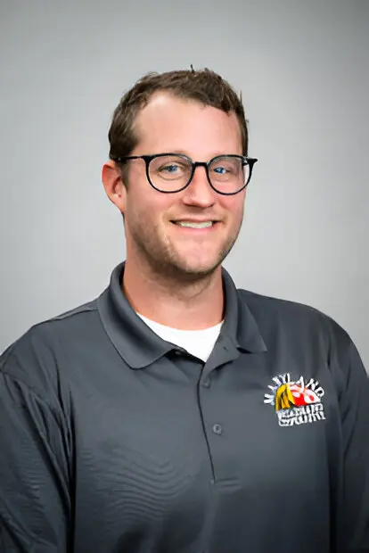 A man wearing glasses and a gray polo shirt with a Maryland State Coral Reef logo stands against a plain backdrop, smiling at the camera, representing Broadband Access initiatives.