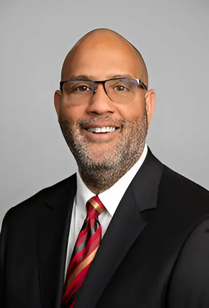 A man with glasses, a beard, and a shaved head is wearing a dark suit, white shirt, and red-striped tie, smiling against a plain background, embodying the confidence of seamless broadband access.